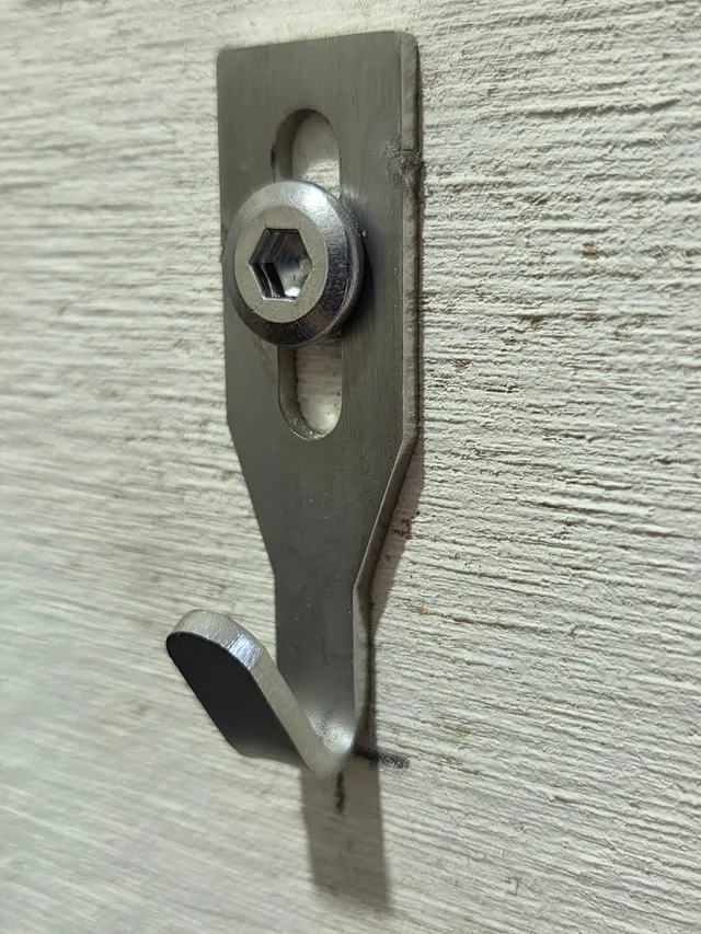 An angled view shows a Centre Hook Small fixed to a textured wall with a hex-socket screw, sitting on the pencil mark.