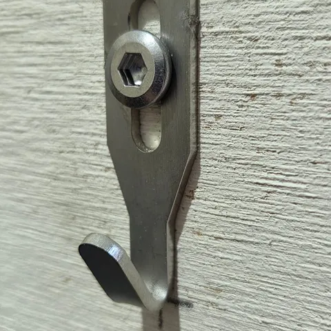 An angled view shows a Centre Hook Small fixed to a textured wall with a hex-socket screw, sitting on the pencil mark.