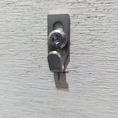 A Centre Hook Stubby is fixed to a textured wall with a stainless hex-socket screw through its slot, on the pencil mark.