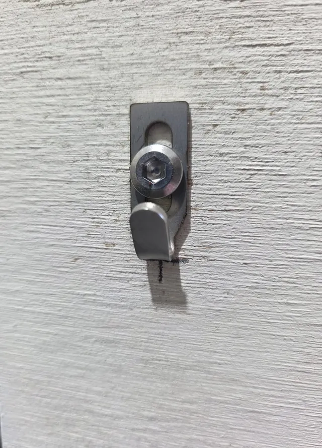 A Centre Hook Stubby is fixed to a textured wall with a stainless hex-socket screw through its slot, on the pencil mark.